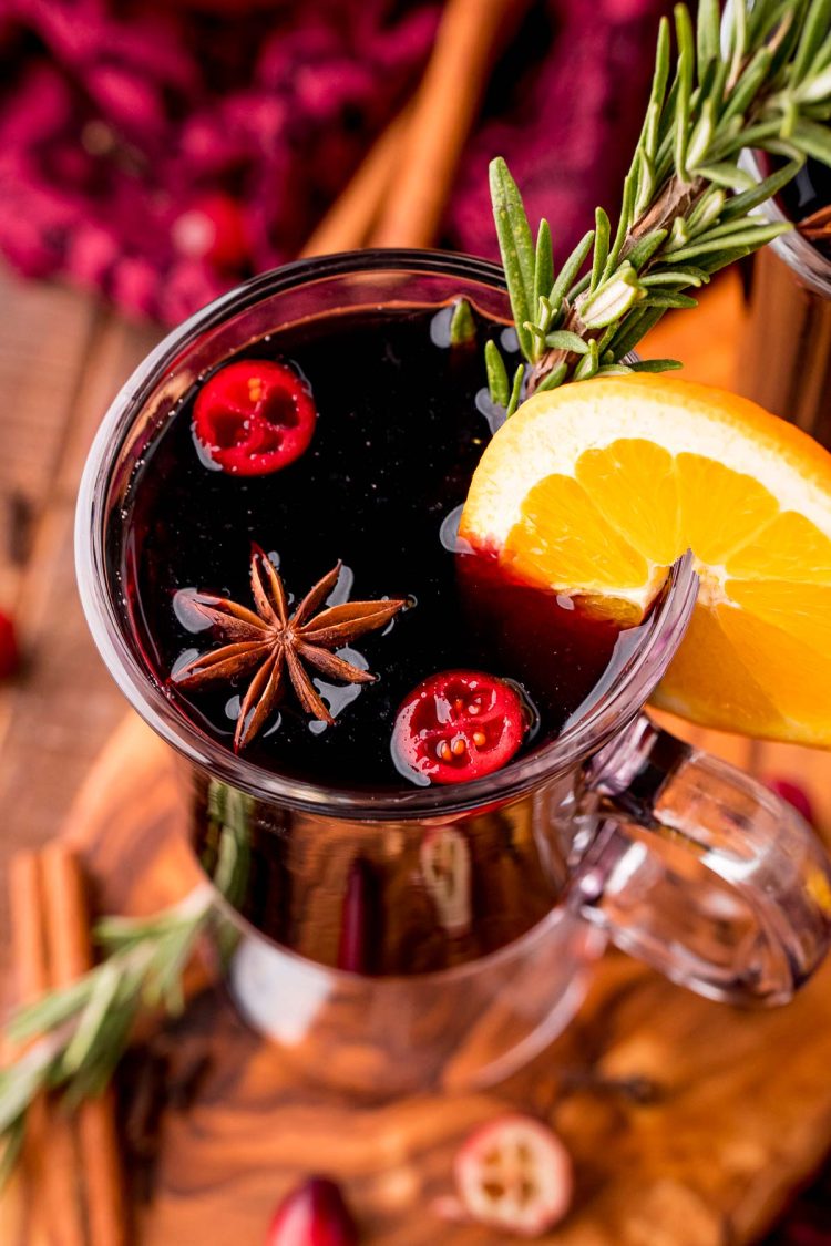 Close up photo of a glass mug filled with mulled wine garnished with rosemary and orange slice.