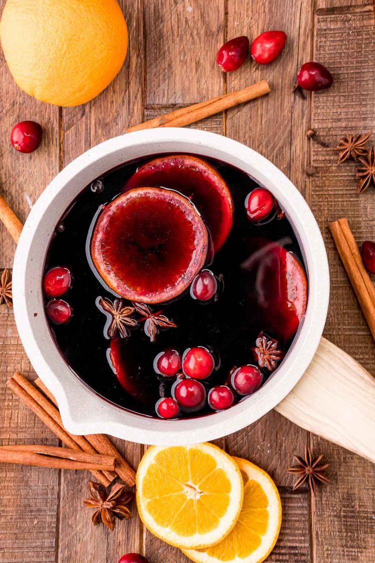 Overhead photo of mulled wine in a small light colored pot with spices and orange slices around it.