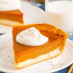 Close up photo of a slice of pumpkin cheesecake pie on a white plate with another slice in the background.