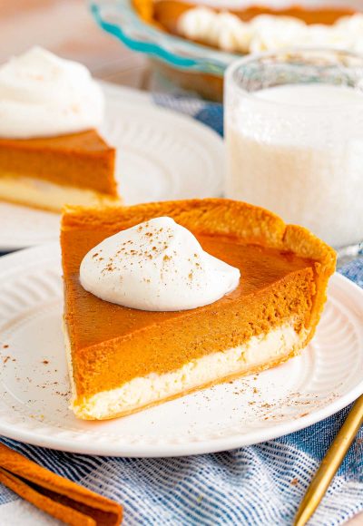 Close up photo of a slice of pumpkin cheesecake pie on a white plate with another slice in the background.