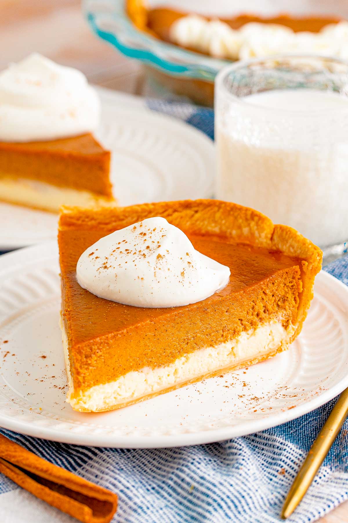 Close up photo of a slice of pumpkin cheesecake pie on a white plate with another slice in the background.