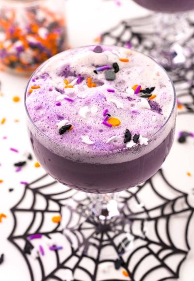 Close up photo of a stemmed glass filled with witch's brew halloween punch on a spider web coaster.