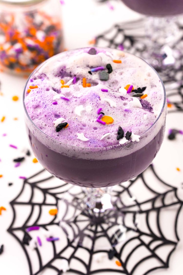 Close up photo of a stemmed glass filled with witch's brew halloween punch on a spider web coaster.
