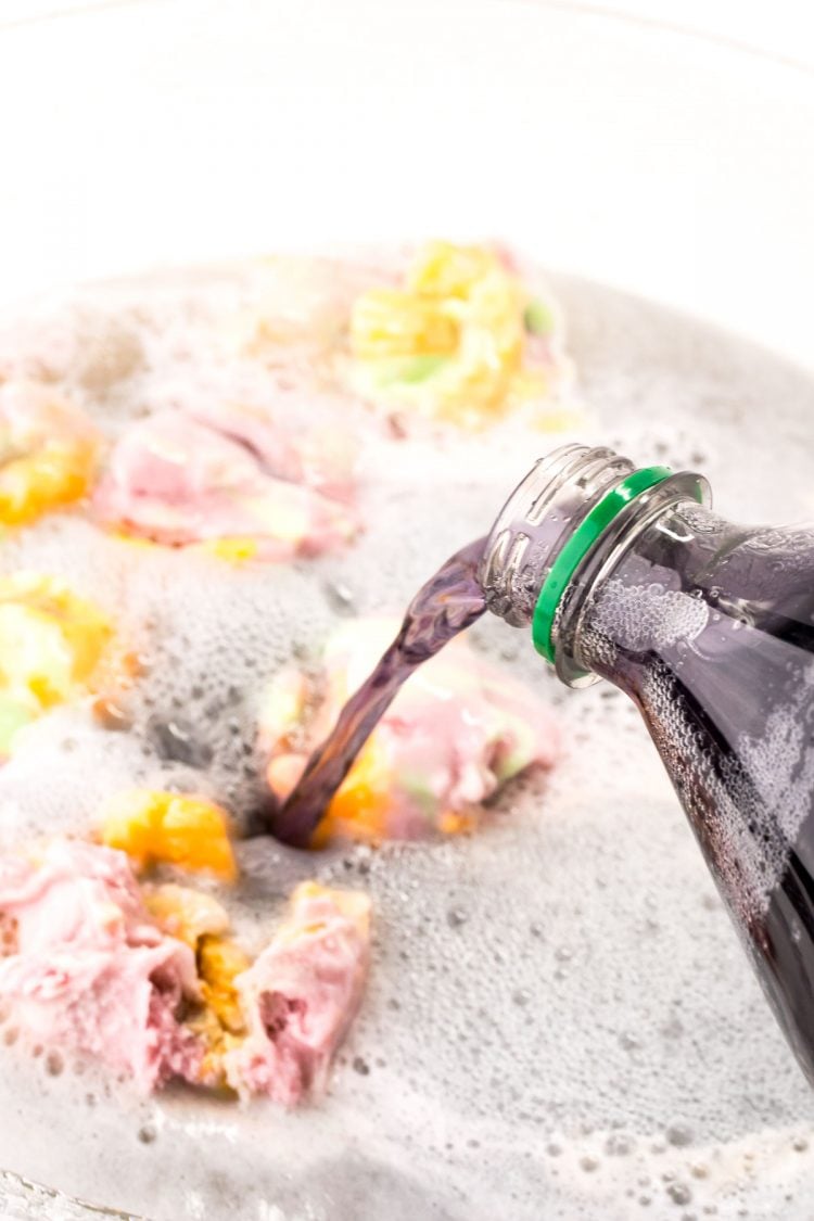 Grape soda being poured into a punch bowl with sherbet and lemonade.