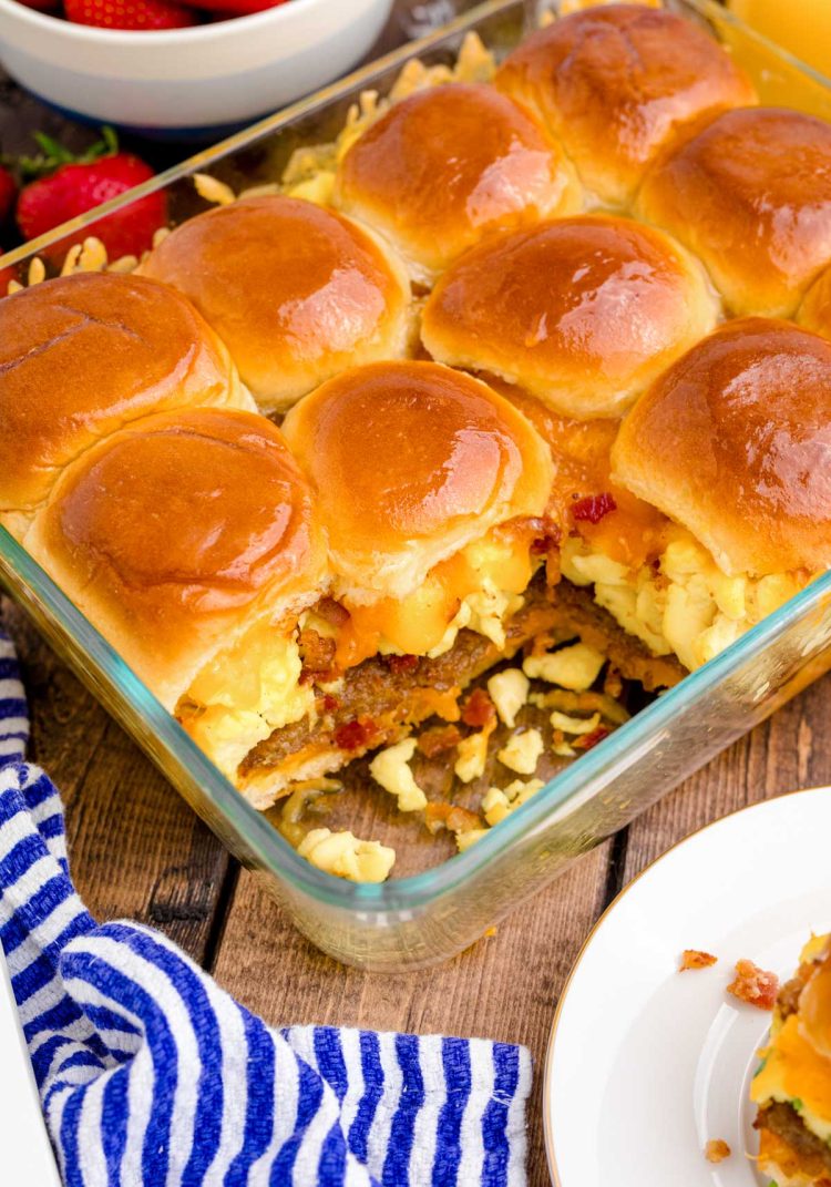 A baking dish of breakfast sliders on a wooden table on a blue and white striped napkin.