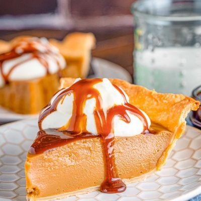 Close up photo of a slice of butterscotch pie on a white plate on a blue napkin.