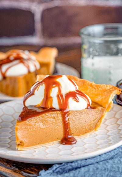 Close up photo of a slice of butterscotch pie on a white plate on a blue napkin.