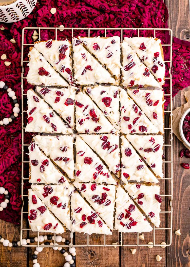 Overhead photo of cranberry bliss bars on a wire rack on a wooden table with a red lace napkin.