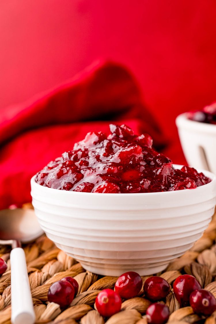 Close up photo of a white bowl of cranberry sauce on a wicker placemat.