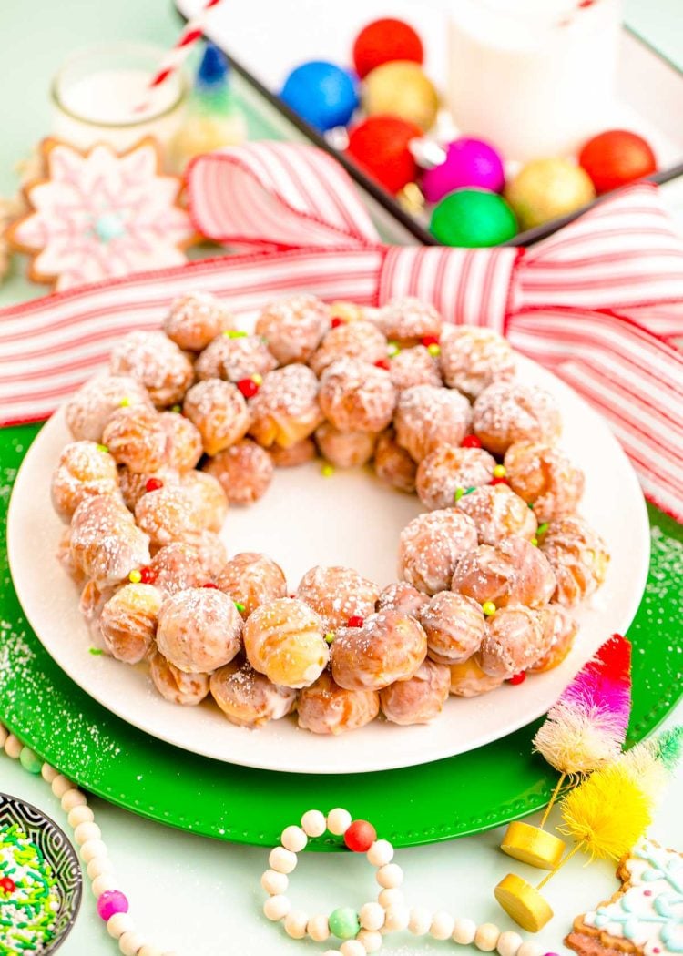 Donut holes arranged on a white plate to look like a wreath with holiday decorations around it.