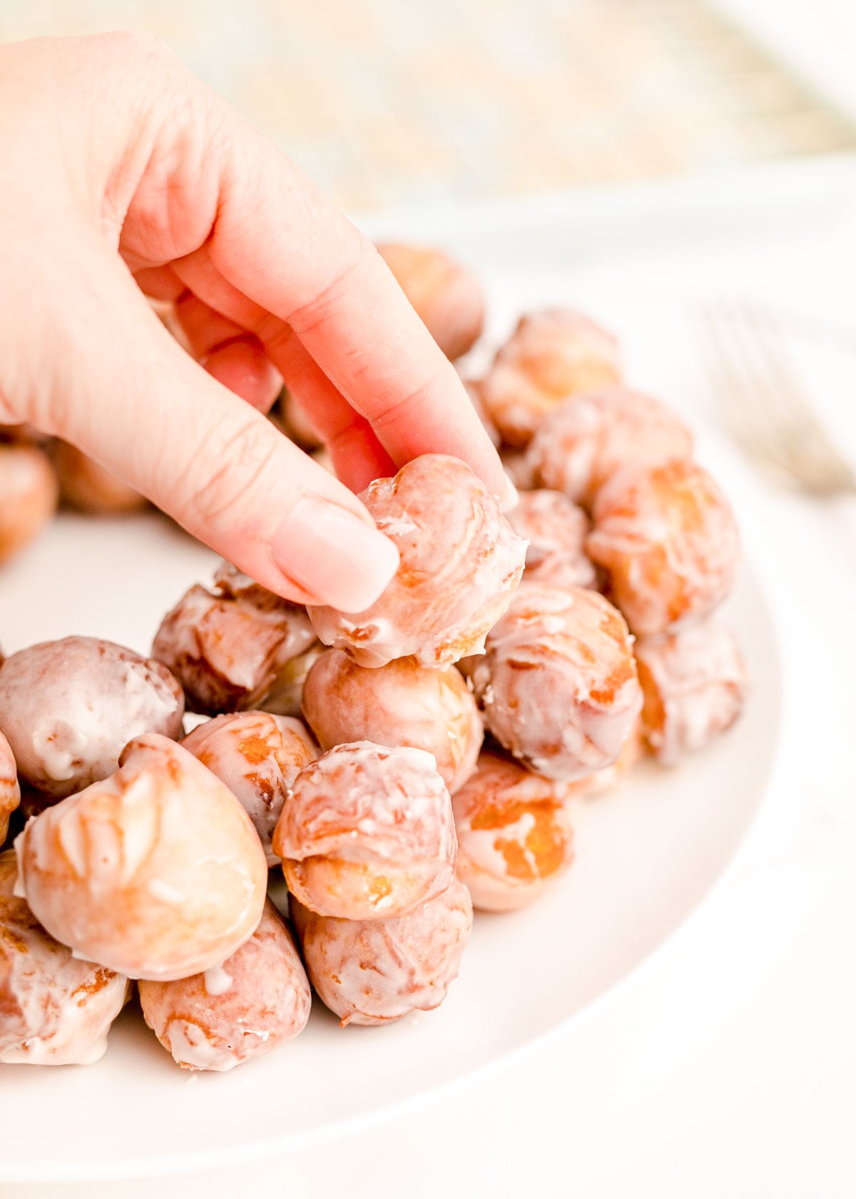 Close up photo of a woman's hand arranging donut holes on a white plate.