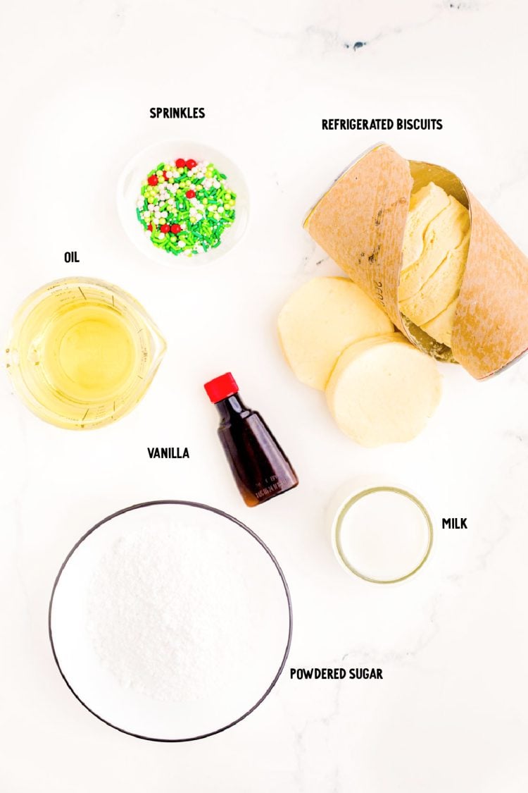 Overhead photo of ingredients prepped to make donut holes from biscuit dough on a white marble surface.