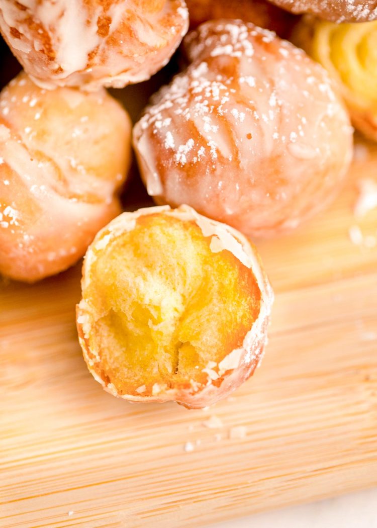 Donut holes on a wooden cutting board with the closest one missing a bite.