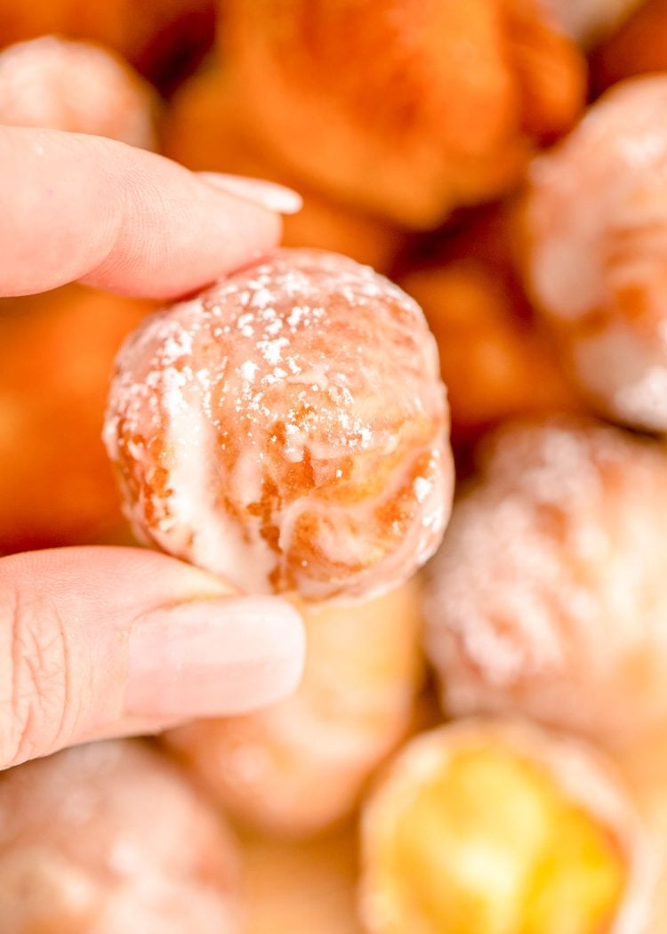 A woman's hand holding a donut hole over a plate with more donut holes.