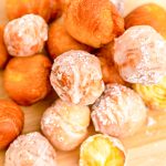 Close up photo of fried donut holes on a wooden cutting board.