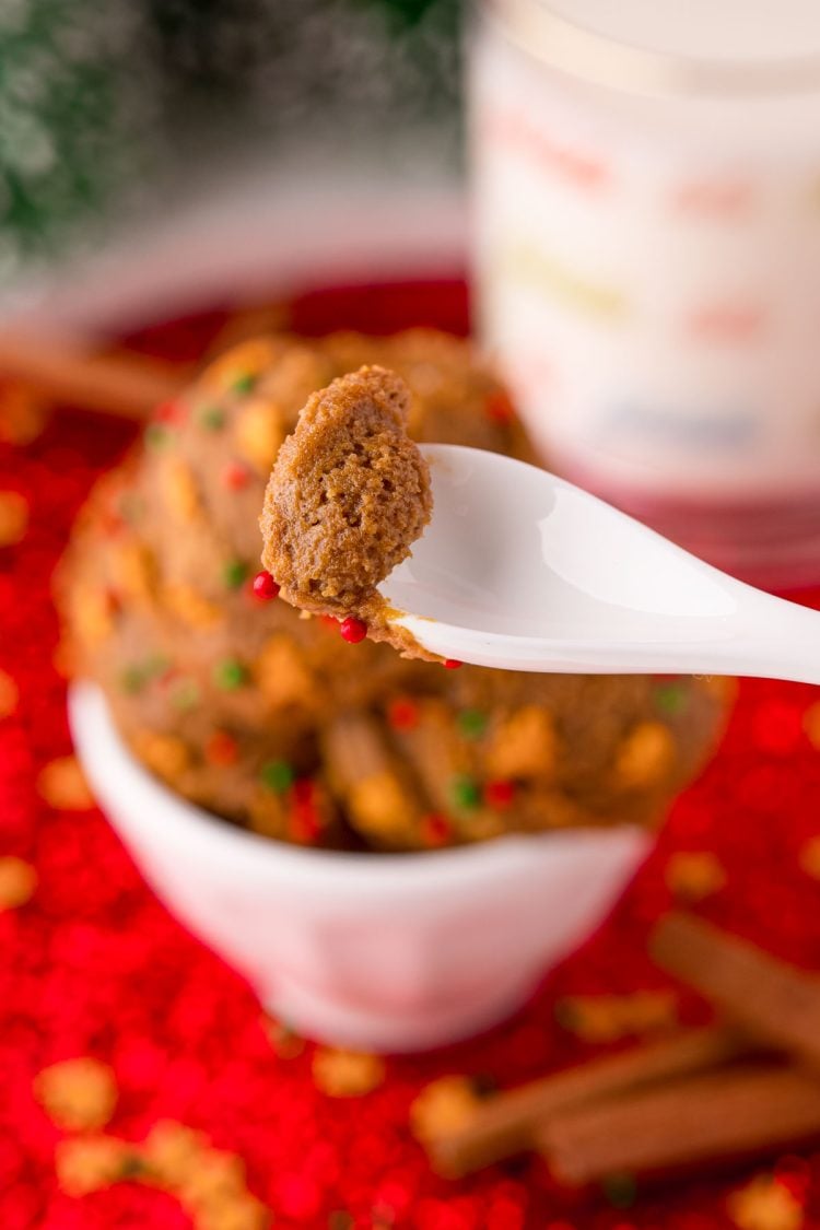 A white spoon taking a bite of edible gingerbread cookie dough from a bowl.