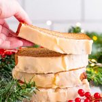 Close up photo of a stack of eggnog bread slices, a woman's hand is taking the top slice off. Holiday decor surrounds the bread.