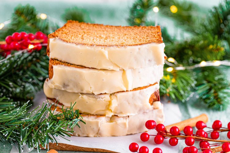 A stack of four slices of eggnog bread on a white plate surrounded by holiday decorations.