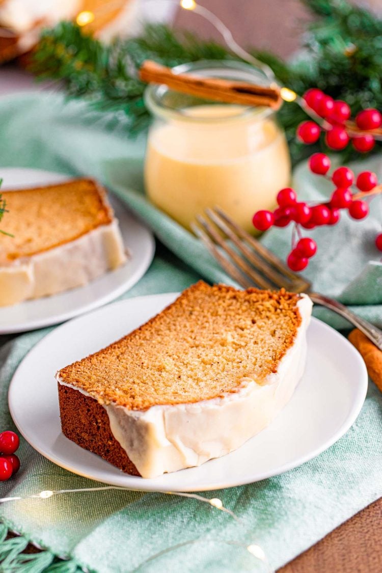 A slice of eggnog quick bread with icing on a white plate on a blue napkin.