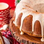 Close up photo of an eggnog pound cake on a wooden cake stand with holiday decorations in the background.