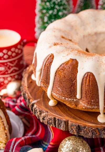 Close up photo of an eggnog pound cake on a wooden cake stand with holiday decorations in the background.