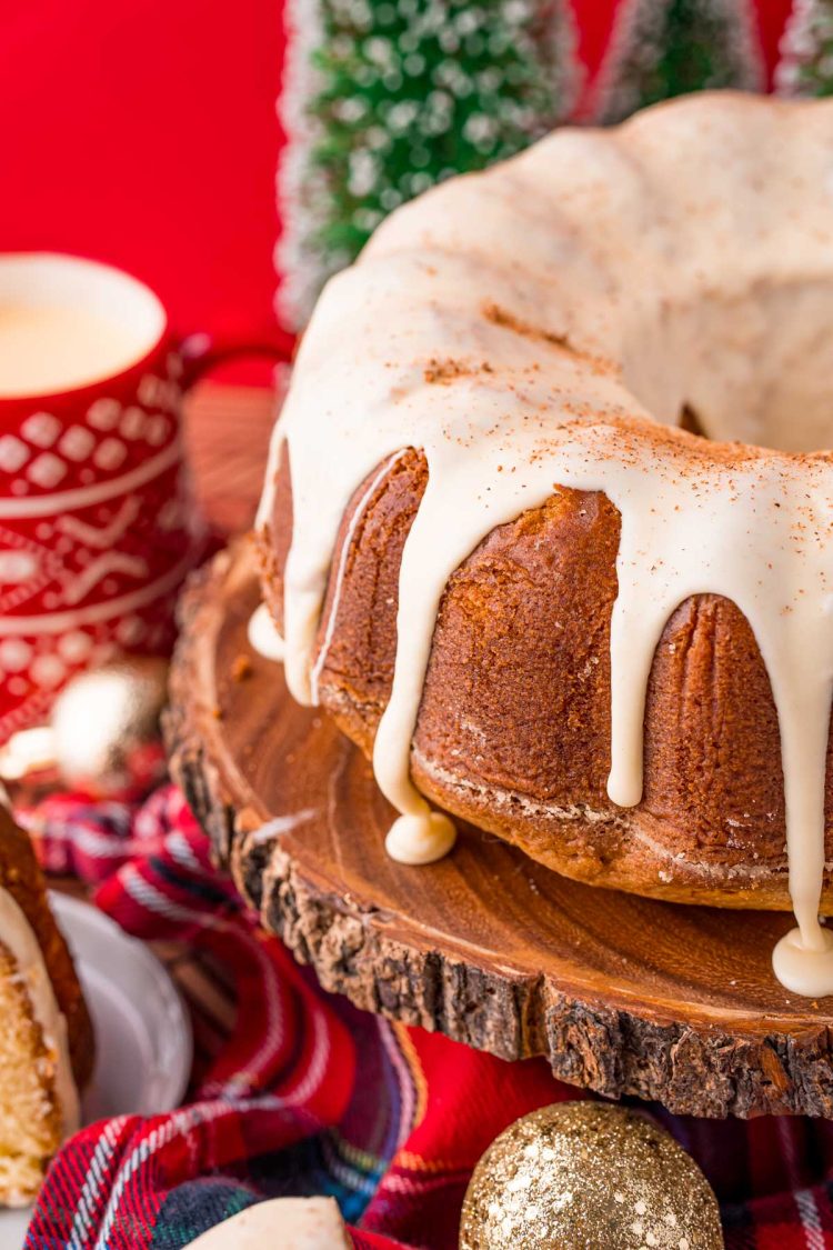 Close up photo of an eggnog pound cake on a wooden cake stand with holiday decorations in the background.