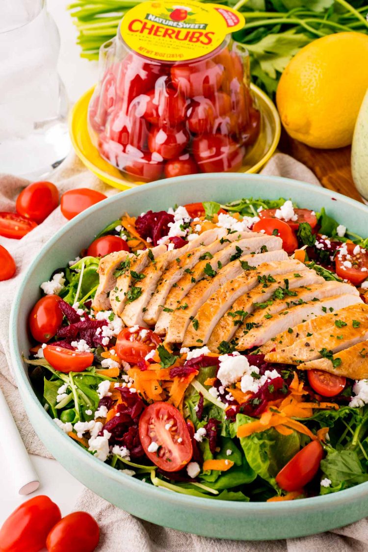 Close up photo of a grilled chicken salad with beets, tomatoes, greens, and goat cheese.