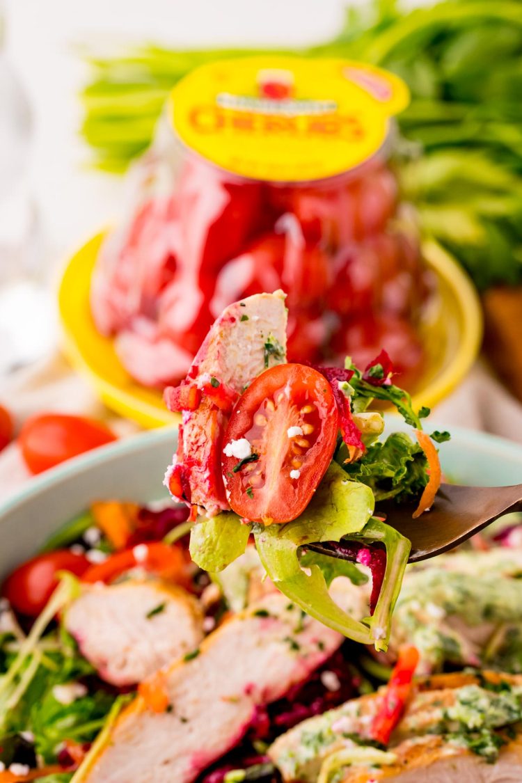 A fork lifting a bite of grilled chicken salad from the bowl.