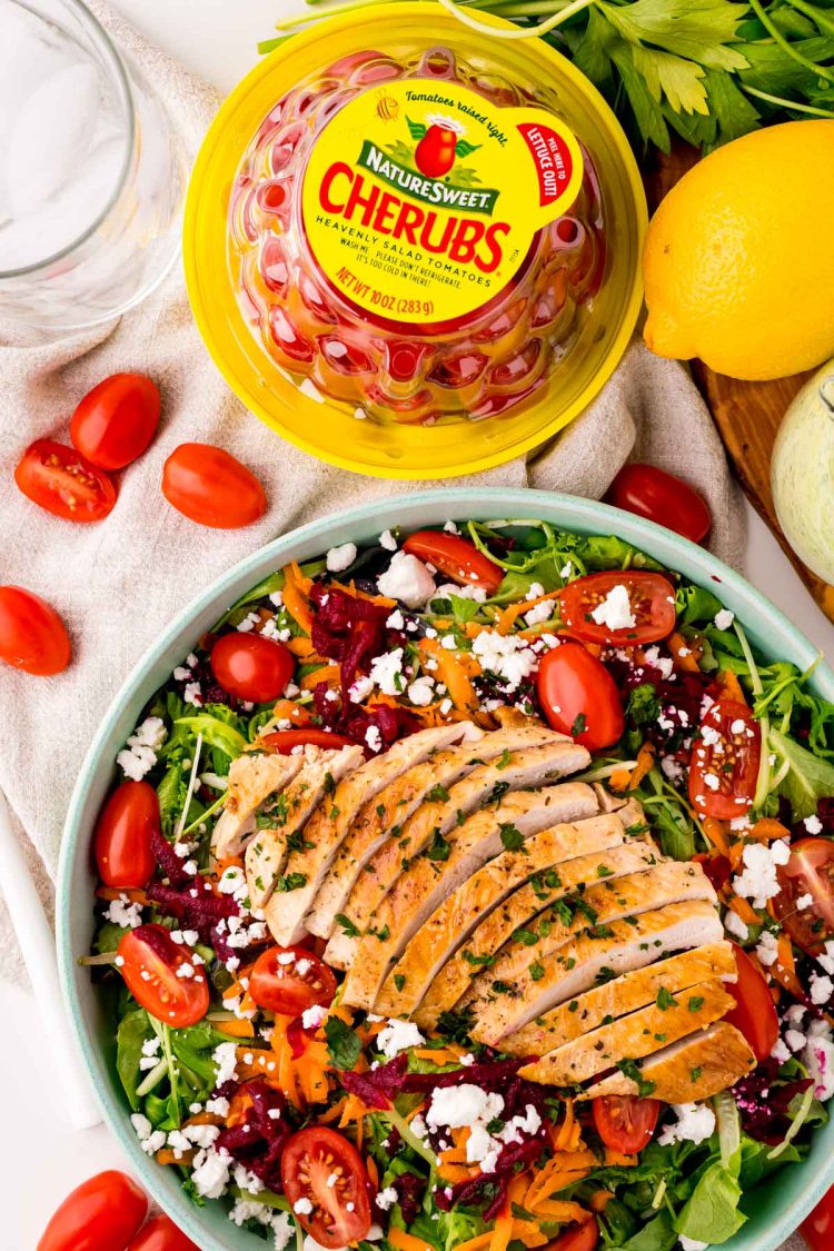 Overhead photo of grilled chicken salad in a teal bowl with a package of NatureSweet Cherubs next to it.