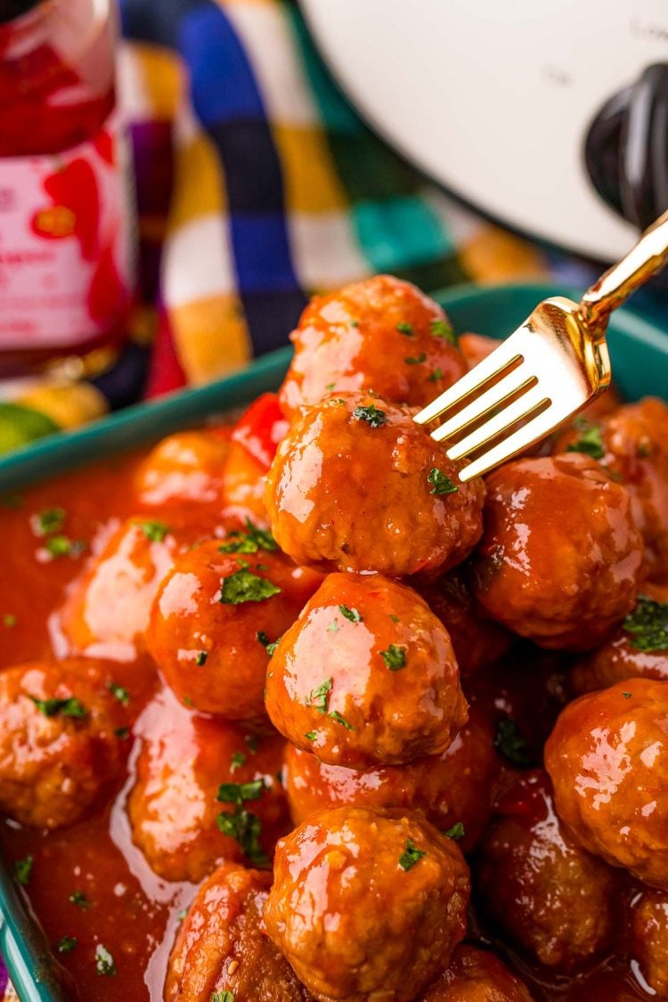 An appetizer fork taking a cocktail meatball off a plate of meatballs.