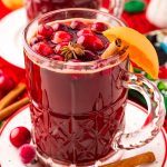 Close up photo of kinder punch in a mug on a white plate surrounded by holiday decorations.