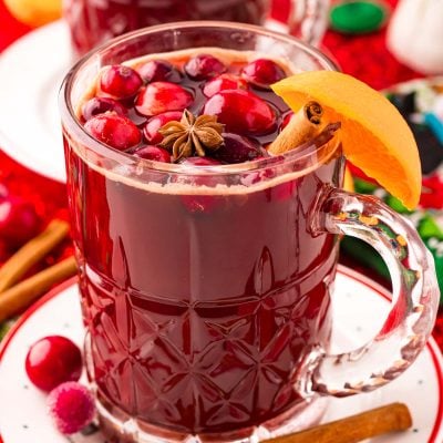 Close up photo of kinder punch in a mug on a white plate surrounded by holiday decorations.