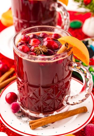 Close up photo of kinder punch in a mug on a white plate surrounded by holiday decorations.