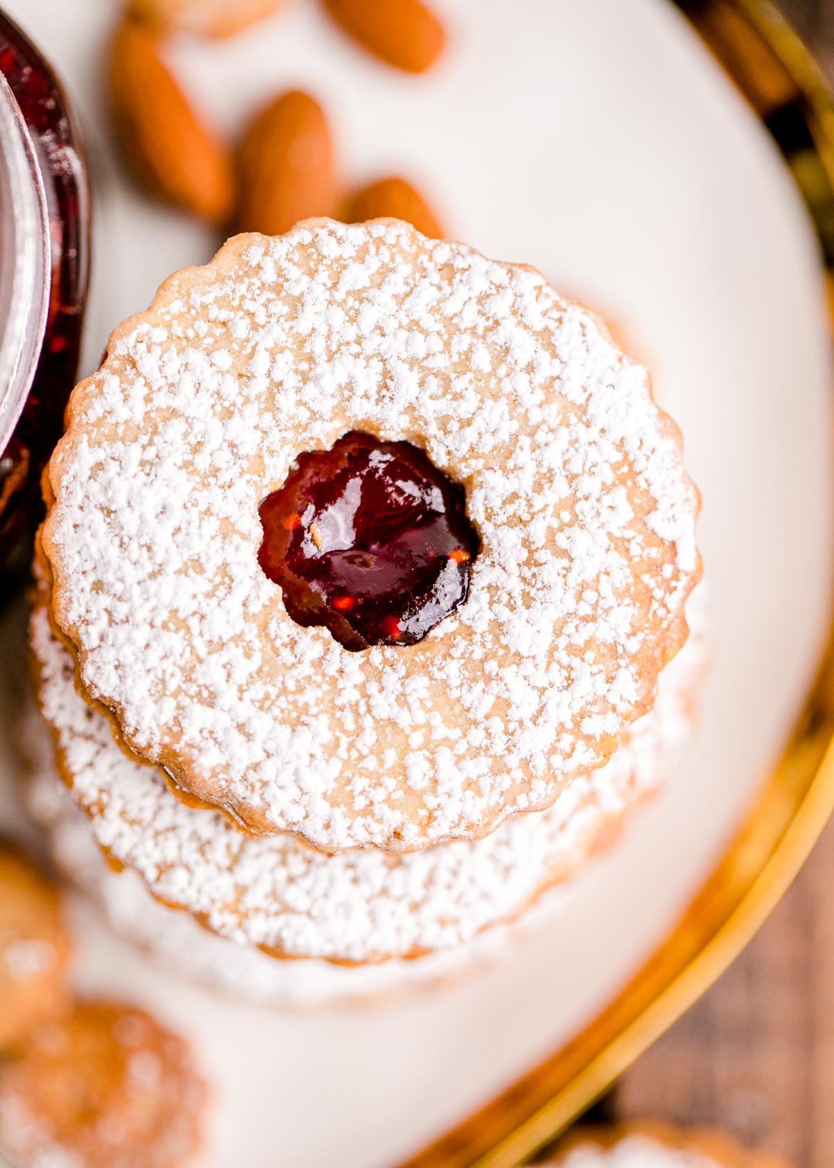 Overhead photo of a stack of linzer cookies on a white plate with a gold trim.