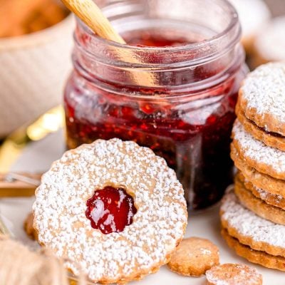 Close up photo of linzer cookies on a plate next to a jar of raspberry jam.