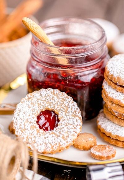 Close up photo of linzer cookies on a plate next to a jar of raspberry jam.