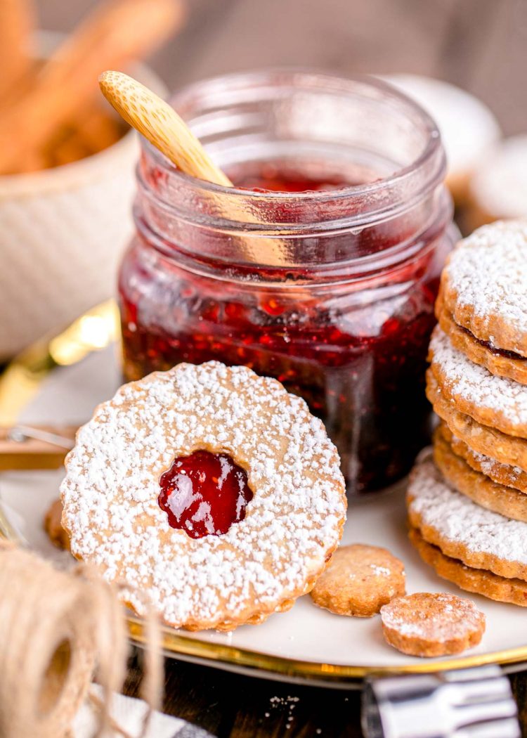 Close up photo of linzer cookies on a plate next to a jar of raspberry jam.