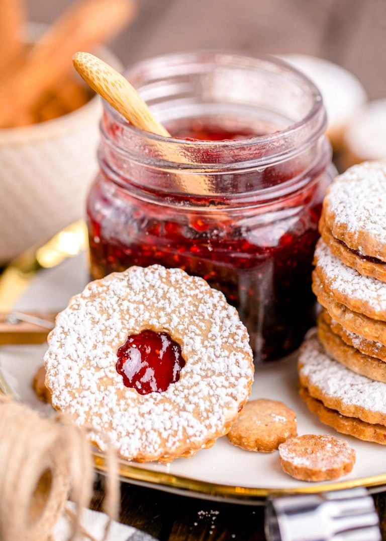 Close up photo of linzer cookies on a plate next to a jar of raspberry jam.