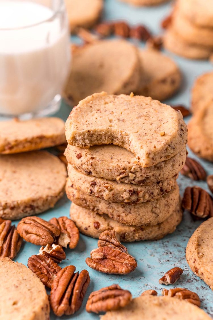 Close up photo of pecan sandies stacked on top of each other with a bite taken out of the top one.