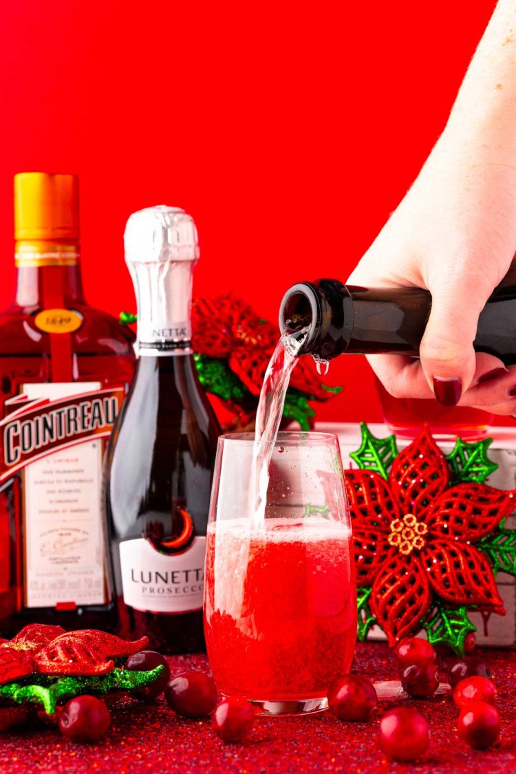 Champagne being poured into a stemless fluted glass to make a poinsettia cocktail.