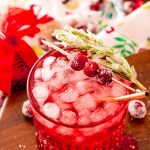 Close up photo of a sparkling vodka cranberry cocktail on a wooden board with holiday decor around it.