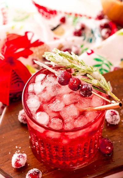 Close up photo of a sparkling vodka cranberry cocktail on a wooden board with holiday decor around it.