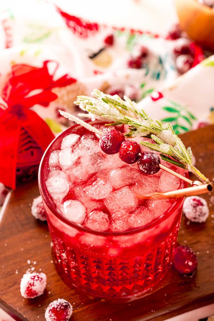 Close up photo of a sparkling vodka cranberry cocktail on a wooden board with holiday decor around it.