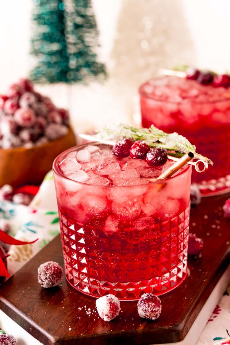 Close up photo of a sparkling vodka cranberry cocktail on a wooden board with holiday decor around it.