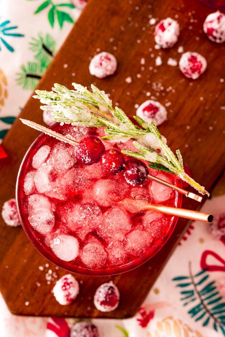 Close up photo of a sparkling vodka cranberry cocktail on a wooden board with holiday decor around it.