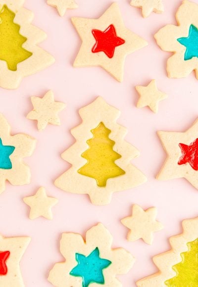 Overhead photo of stained glass christmas cookies on a light pink surface.