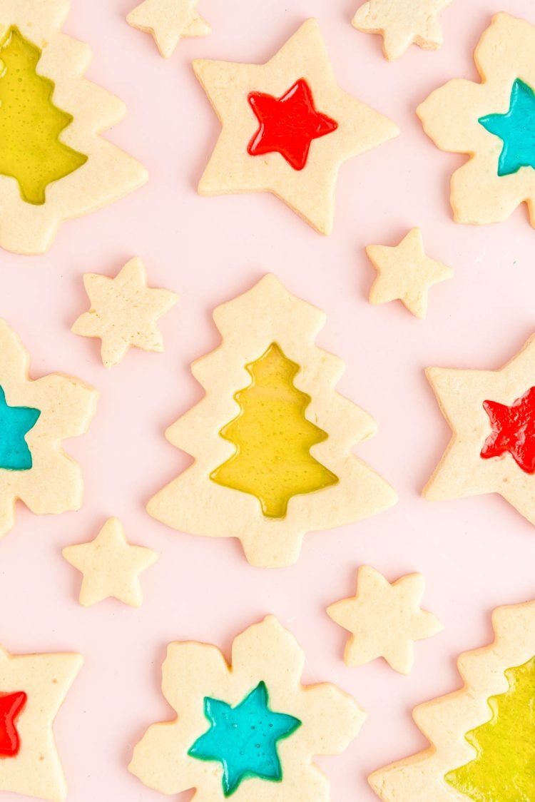 Overhead photo of stained glass christmas cookies on a light pink surface.