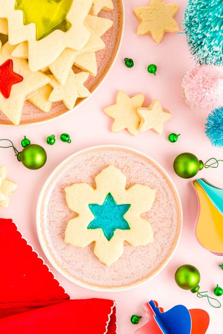 Overhead photo of stained glass cookies on pink plates with a red napkin and holiday decorations scattered around.