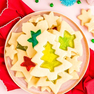 Overhead photo of stained glass sugar cookies on a pink plate on a red napkin.