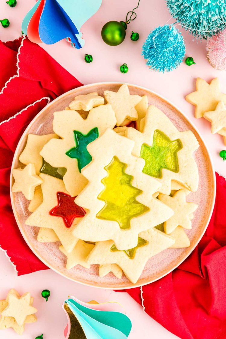 Overhead photo of stained glass sugar cookies on a pink plate on a red napkin.